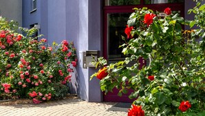 Exterior del INVITE Hotel en Kaisarburg, con una entrada destacada que incluye una puerta de cristal, un cartel sobre la entrada y un jardín bien cuidado con rosas rojas.