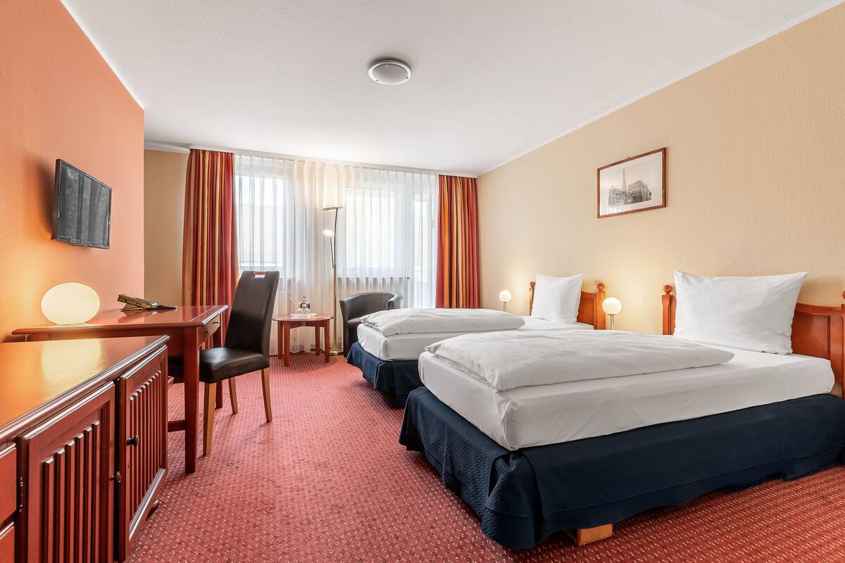 Una habitación de hotel con dos camas, un escritorio, una silla, un televisor y un cuadro en la pared.
