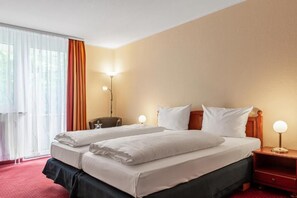 Habitación de hotel con dos camas, un escritorio, una silla y una mesita de noche con lámpara.