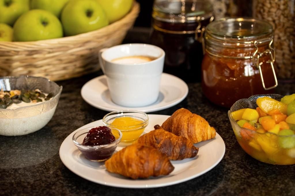 Desayuno con cruasanes, fruta, mermelada y miel en un plato.