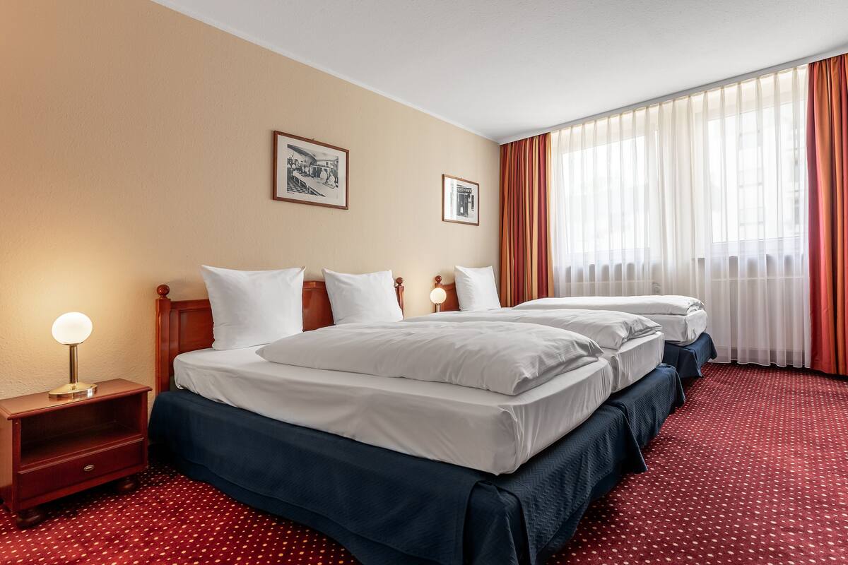 Una habitación de hotel con dos camas, una mesita de noche con lámpara y una alfombra roja con lunares.