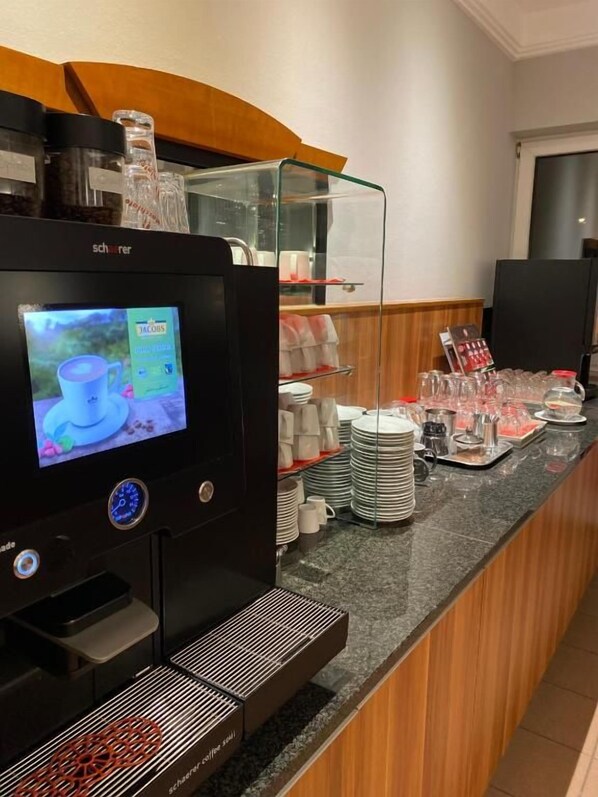 Una estación de café con pantalla digital, dispensadores de café y una variedad de tazas y platillos.