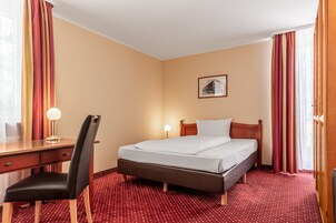 Una habitación de hotel con cama, escritorio, silla y una alfombra roja con estampado.