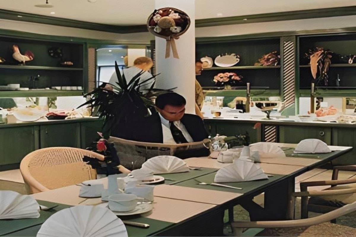 Un coin repas avec une table dressée pour deux personnes, un ventilateur de plafond et des étagères ornées d’objets décoratifs.