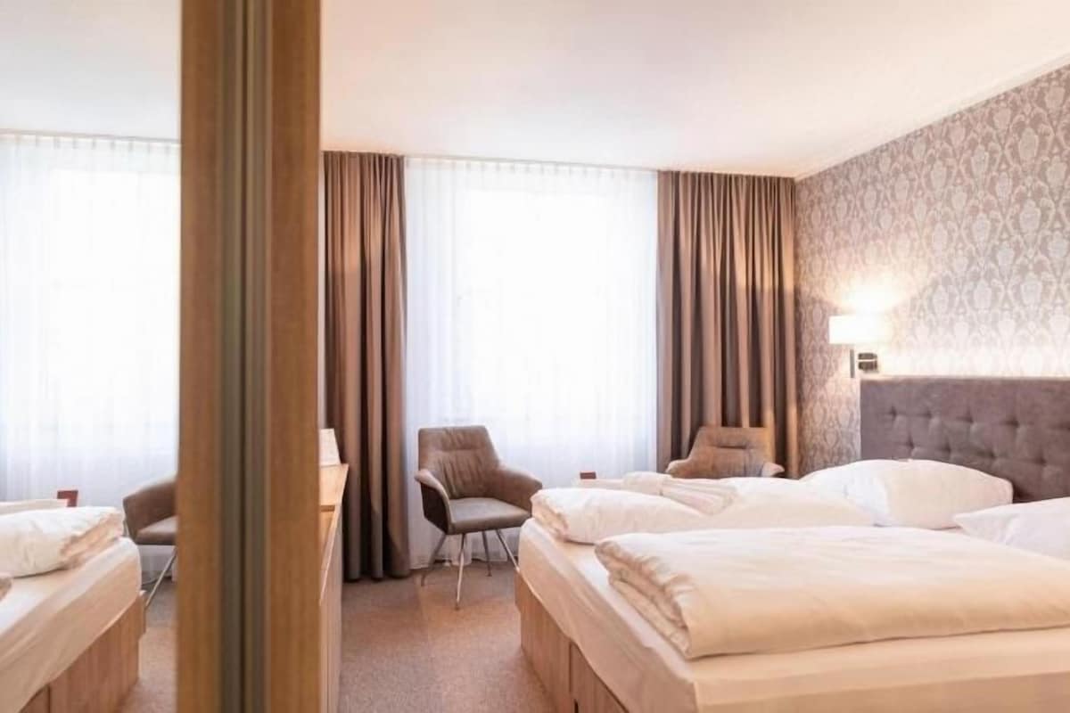 Une chambre d’hôtel avec deux lits, un bureau, une chaise et une grande fenêtre avec des rideaux.