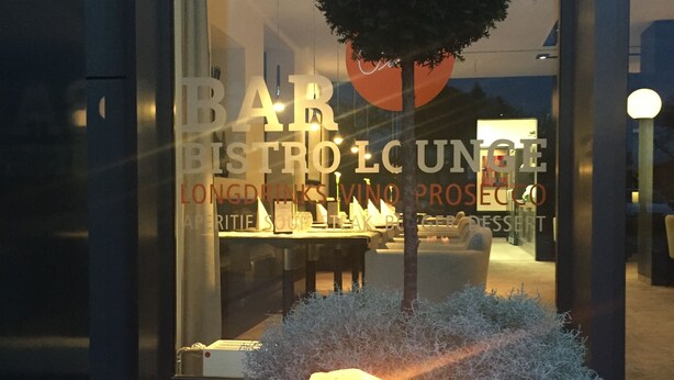 A bar and restaurant with a glass facade, a tree planter with a tree, and a lit candle. - Hotel Schempp (Bobingen)