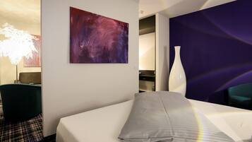 Habitación de hotel con cama, un cuadro abstracto grande, un jarrón blanco y una lámpara moderna.