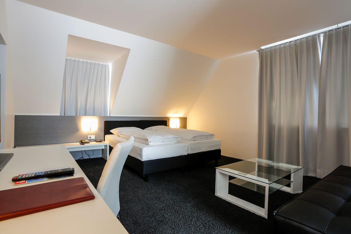 A hotel room with a bed, bedside table, lamp, and a small glass table.
