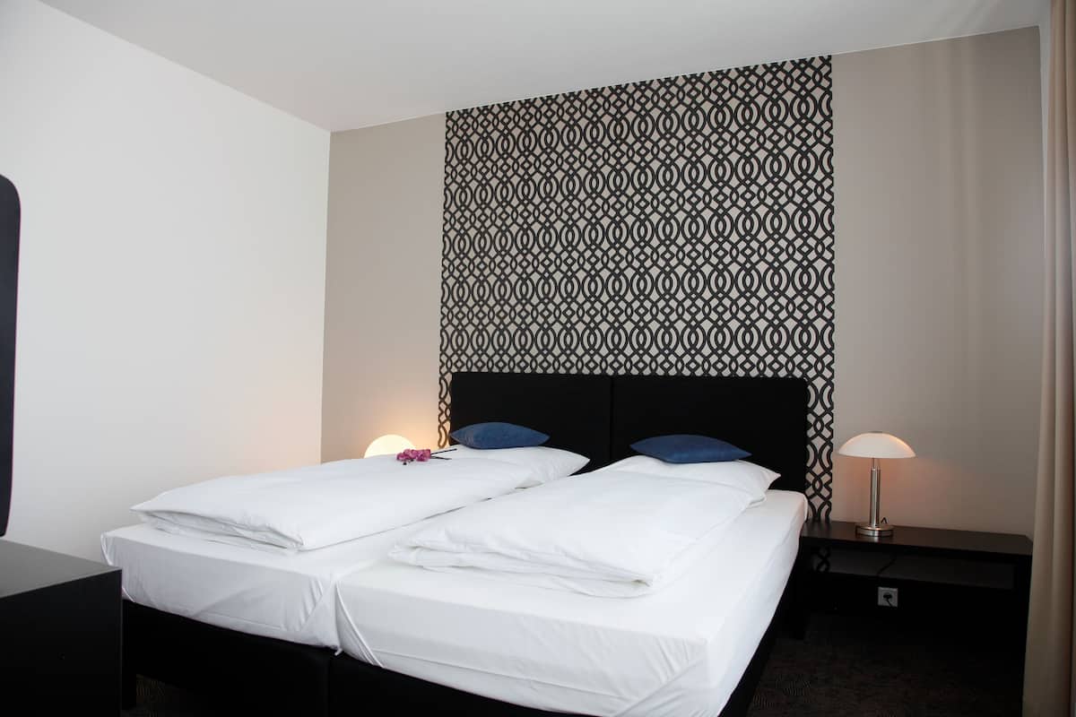 A hotel room with two beds, a patterned headboard, bedside lamps, and a nightstand.