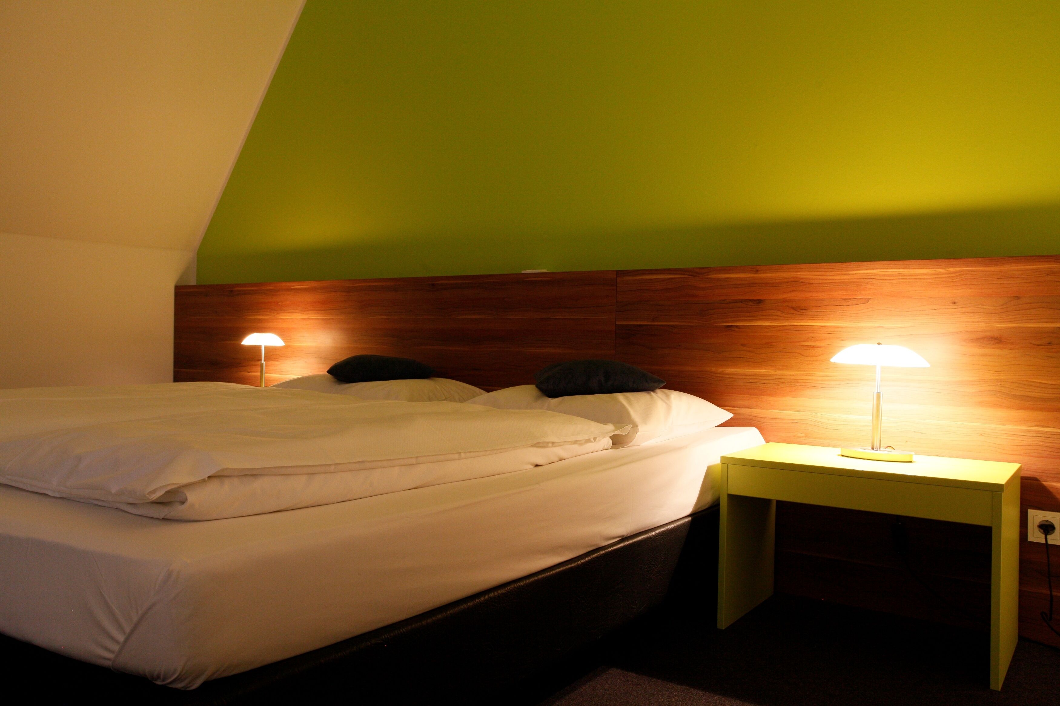Ein ordentlich bezogenes Bett mit weißen Leinen und zwei Kissen, ein hölzernes Kopfteil und ein Nachttisch mit einer Lampe.