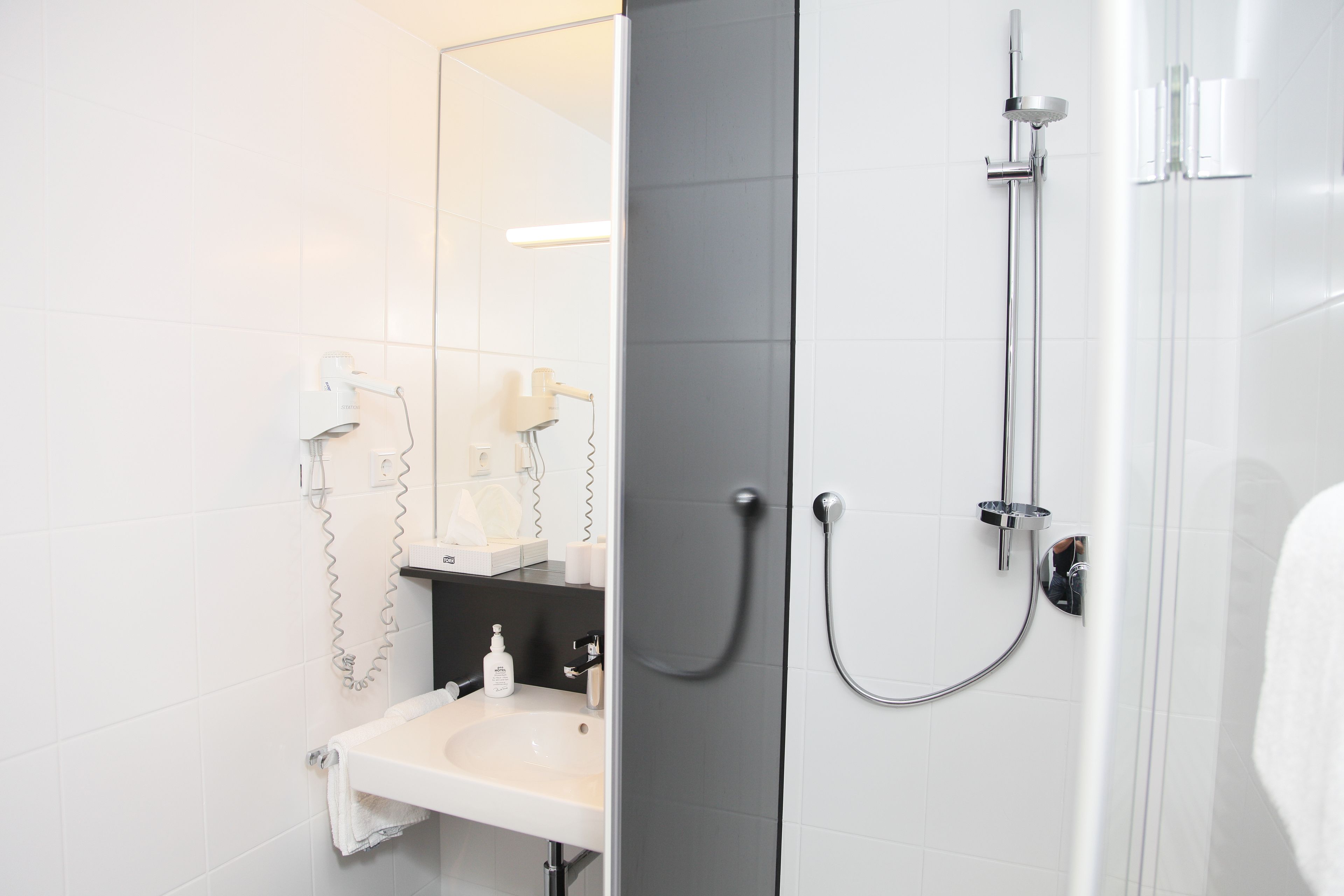 Een moderne badkamer met een witte wastafel, een spiegel en een douche met een handdouche.