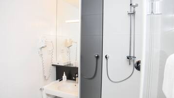 A modern bathroom with a white sink, a mirror, and a shower with a handheld showerhead.
