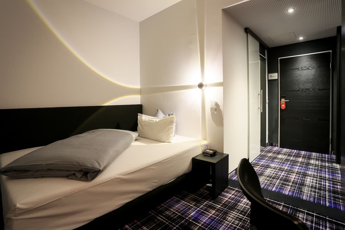 A hotel room with a bed, bedside table, and a chair.