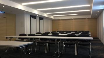 Un salón de conferencias con largas mesas y sillas, piso alfombrado e iluminación empotrada en el techo.