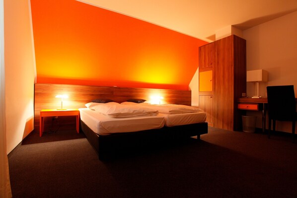 A hotel room with a large bed, two bedside tables with lamps, a desk, and a chair.