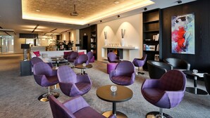 A modern lounge area with purple chairs, round tables, and a fireplace. - Hotel Schempp (Bobingen)