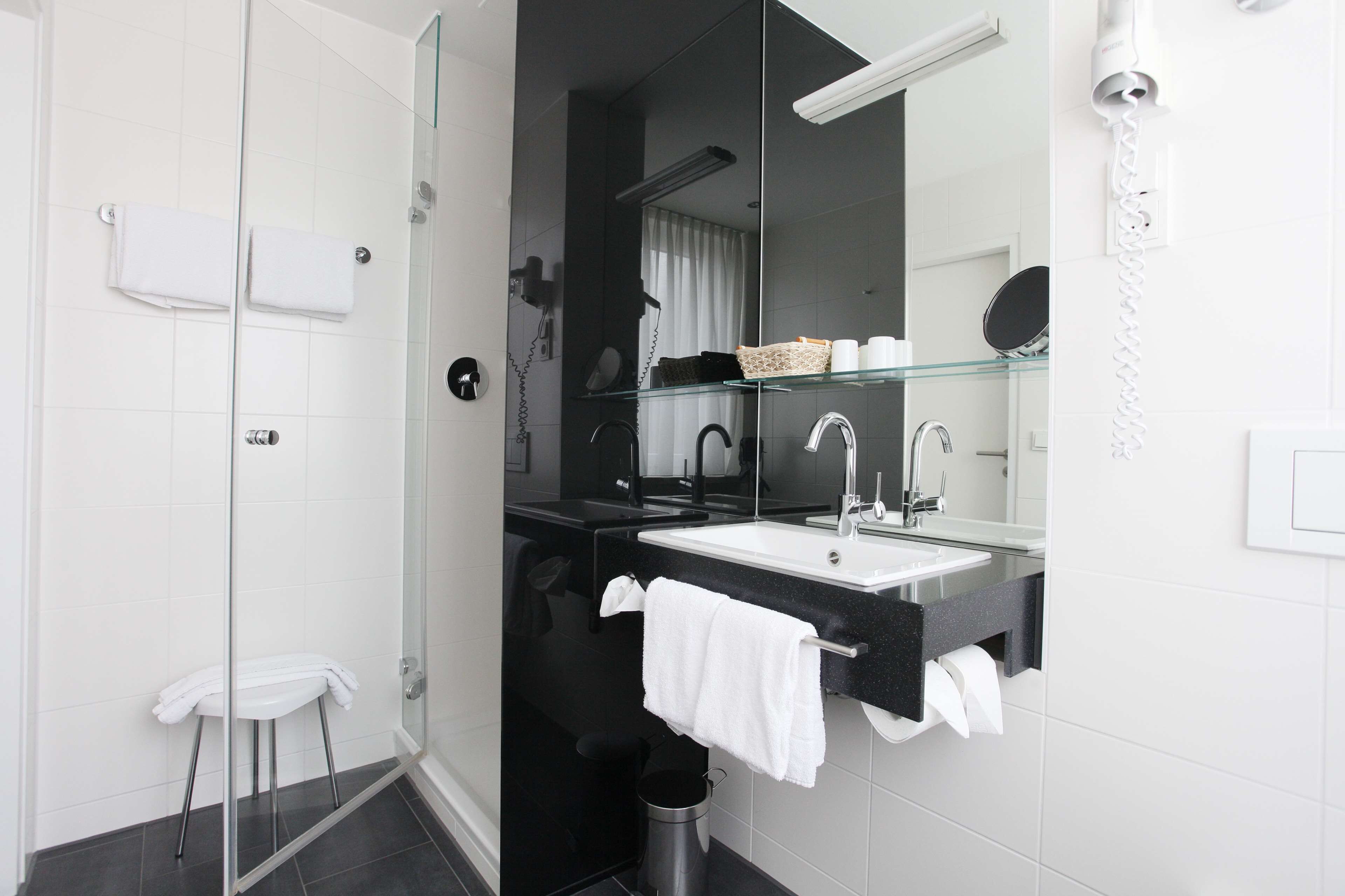 A modern bathroom with a glass shower enclosure, a black countertop sink, and a large mirror.