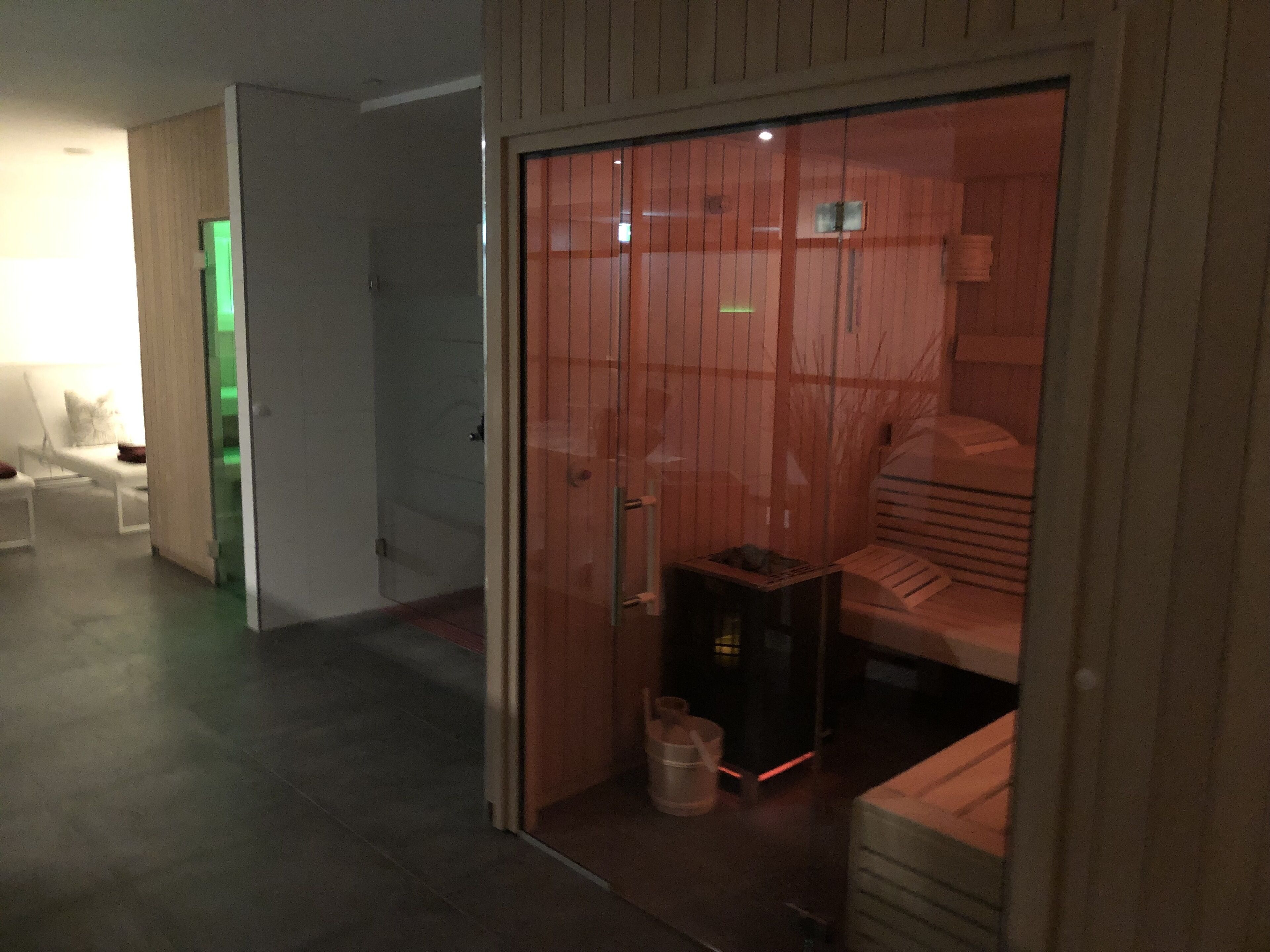 A room with a sliding door leading to a bed area, a small table with a lamp, and a bucket.