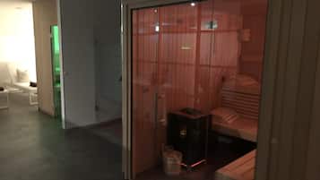 A room with a sliding door leading to a bed area, a small table with a lamp, and a bucket.