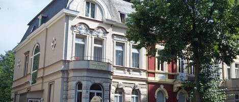 A multi-story building with a classic architectural style, featuring a prominent balcony and a staircase leading to the entrance.
