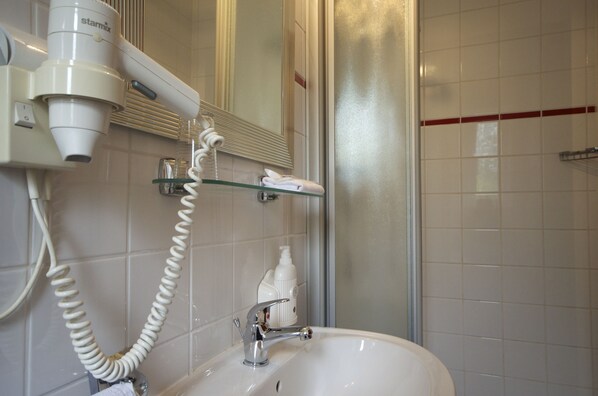 A bathroom with a white sink, a hairdryer, and a glass shelf with a towel.