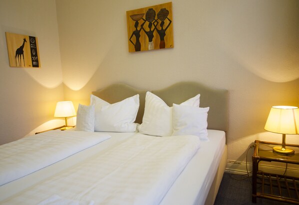 A hotel room with two beds, a headboard, bedside lamps, and artwork on the walls.