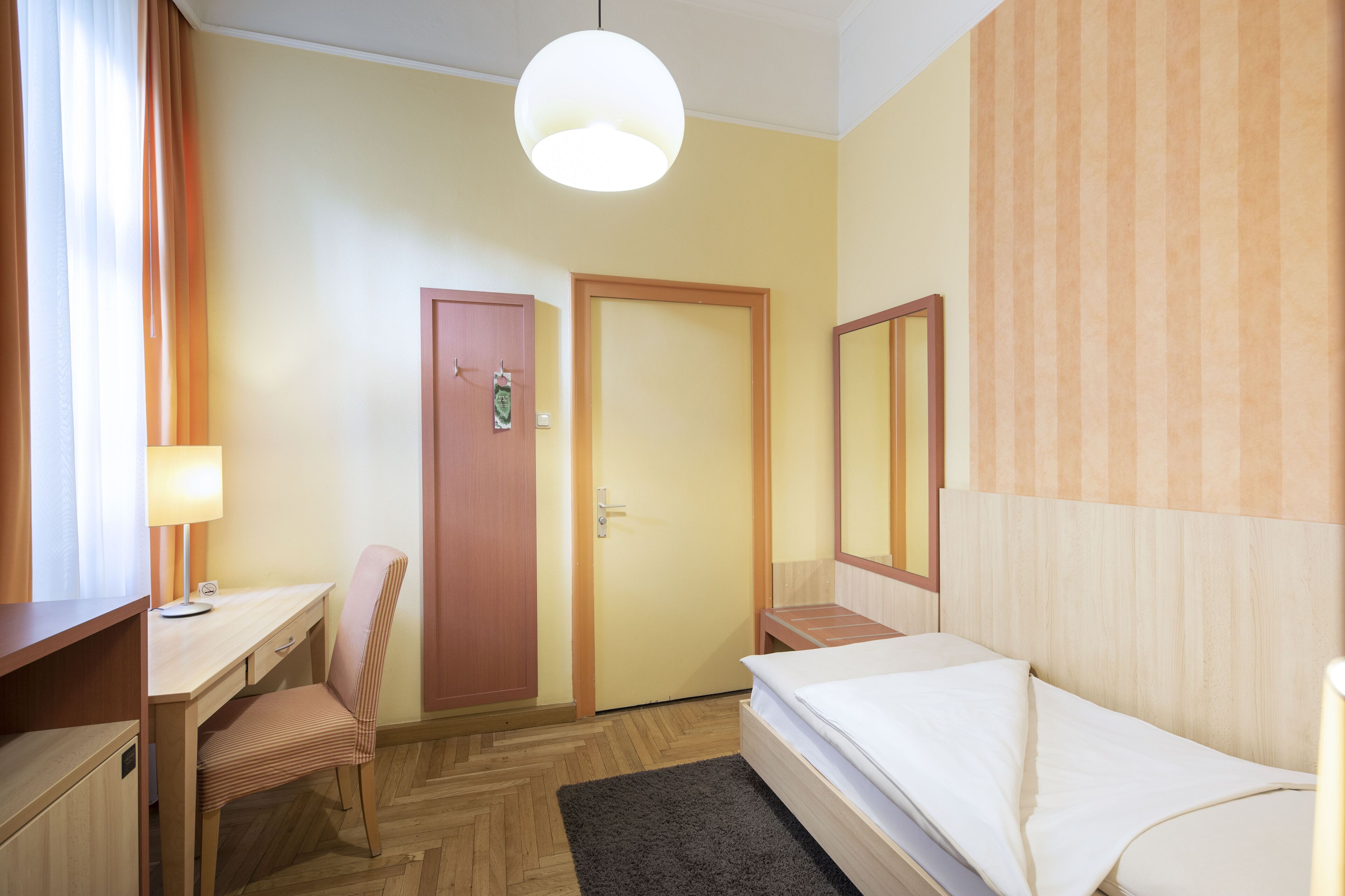 Habitación de hotel con un escritorio de madera, una silla, una cama, una puerta y un espejo grande.