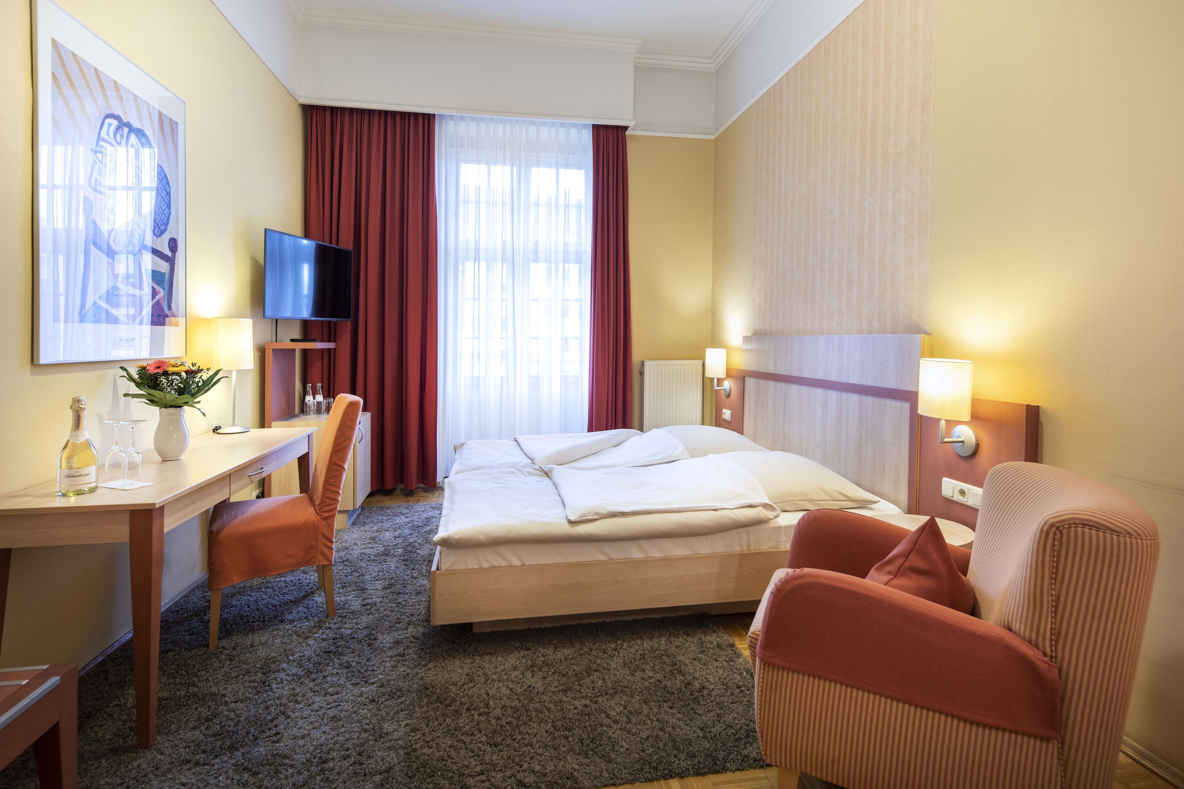Ein Hotelzimmer mit Bett, Schreibtisch mit Stuhl, Fernseher und einem fenster mit Vorhängen.