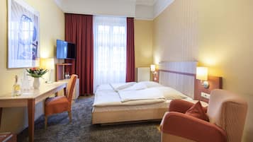 Ein Hotelzimmer mit Bett, Schreibtisch mit Stuhl, Fernseher und einem fenster mit Vorhängen.