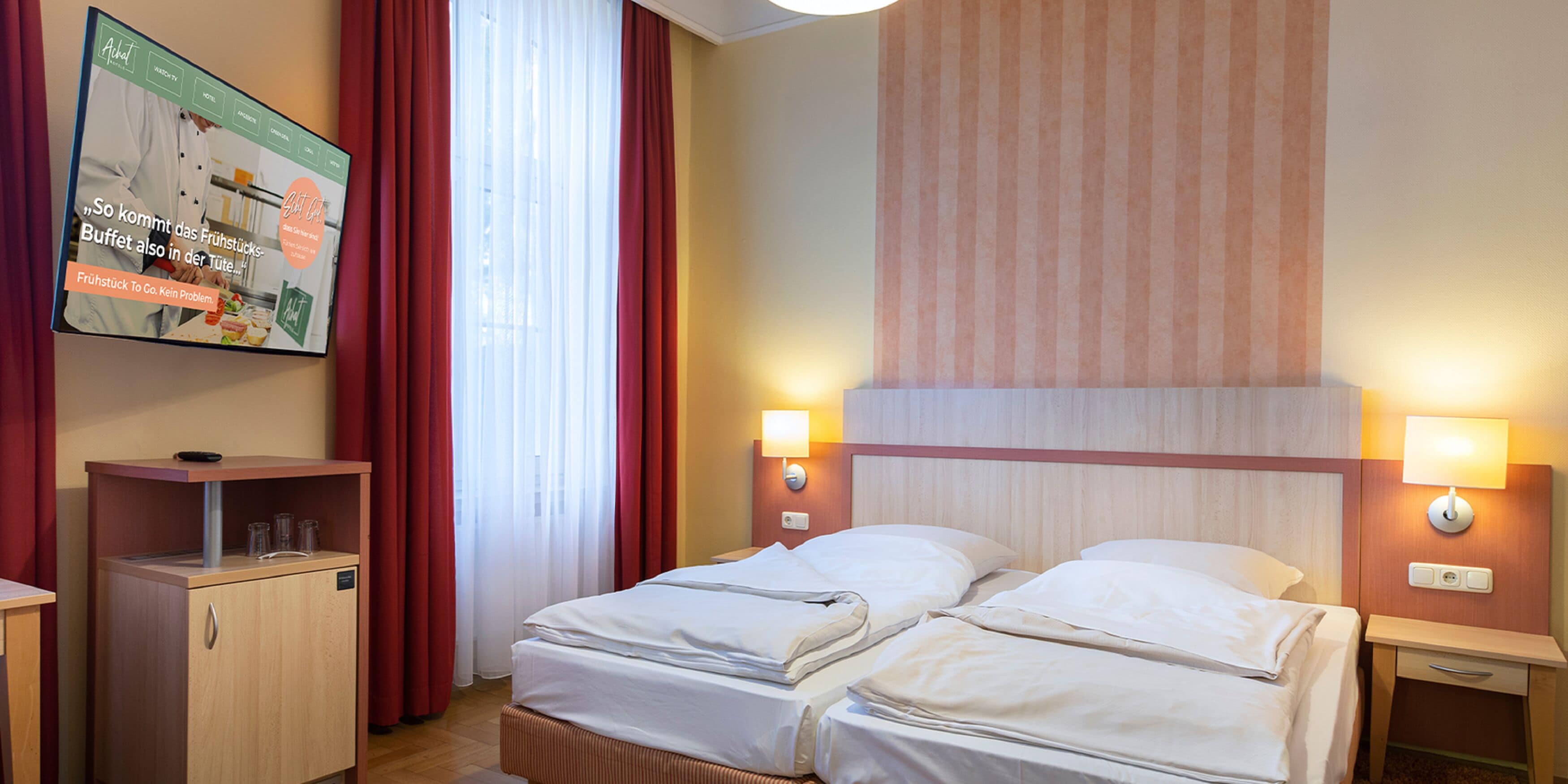 A hotel room with two beds, a TV mounted on the wall, and a wooden cabinet.