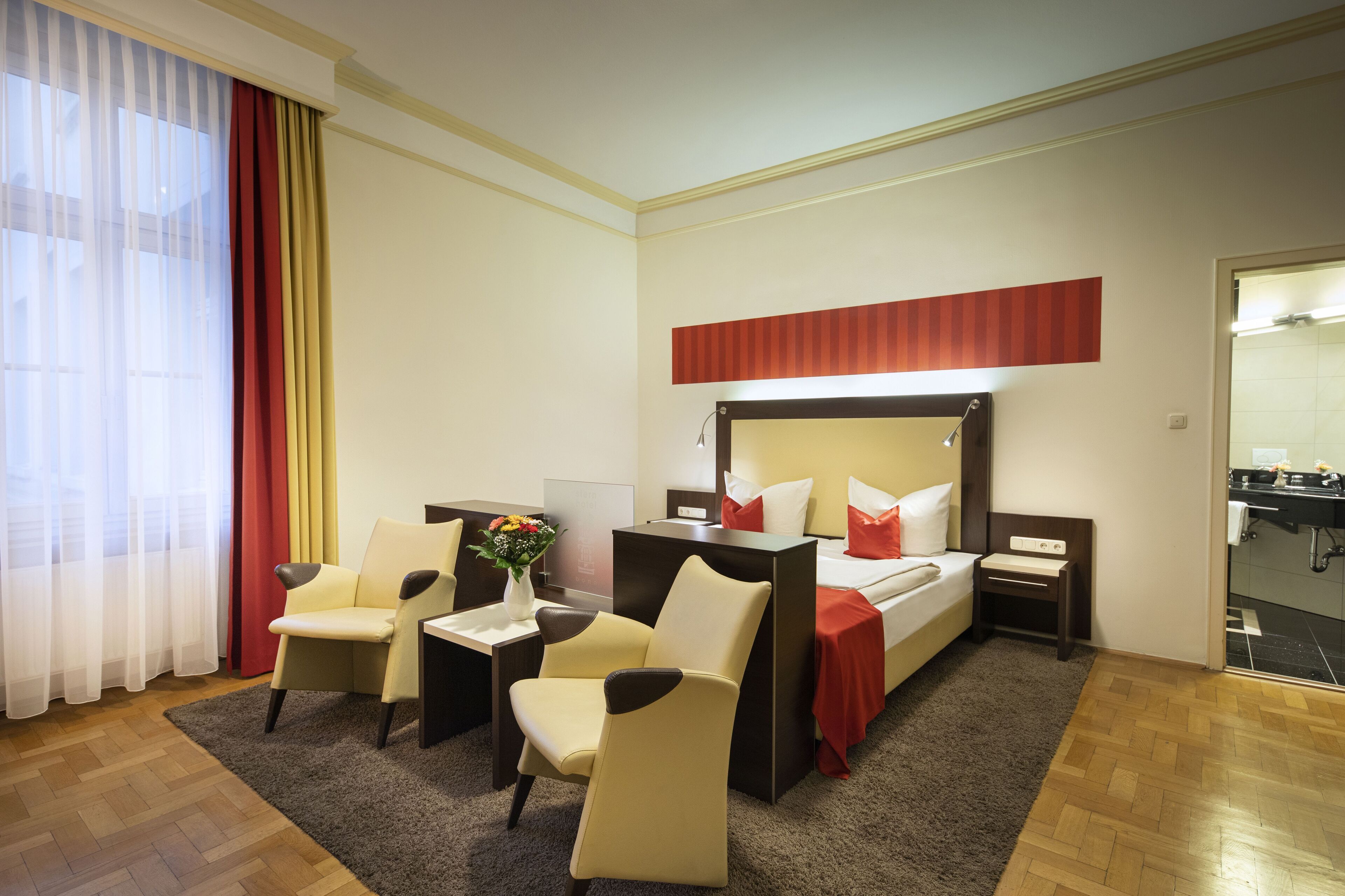 A hotel room with a bed, two chairs, a desk, and a bathroom visible through an open door.