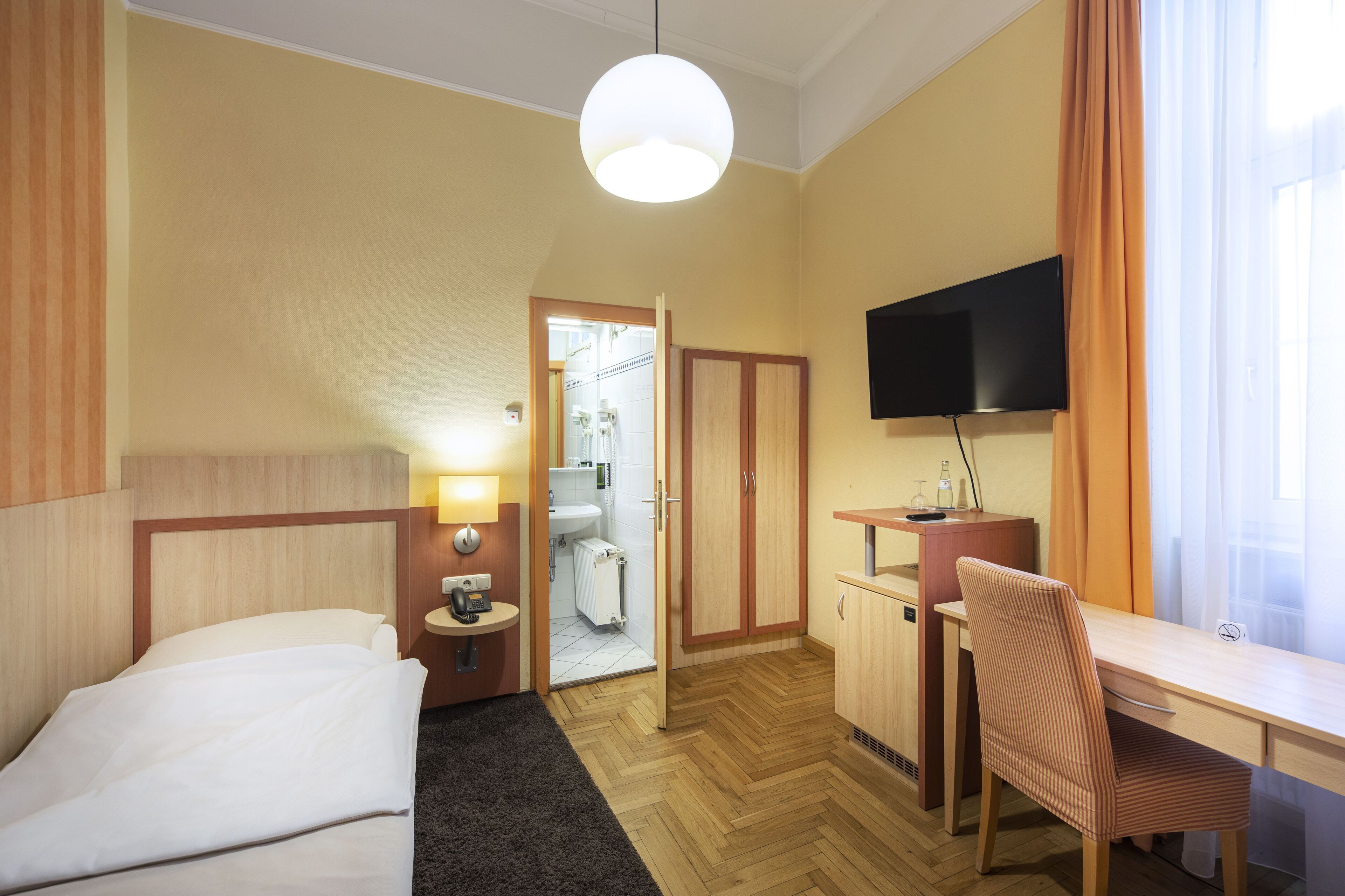 Habitación de hotel con cama, escritorio, silla, televisión y baño visible a través de una puerta abierta.