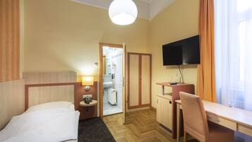Habitación de hotel con cama, escritorio, silla, televisión y baño visible a través de una puerta abierta.