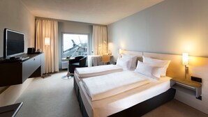 Habitación de hotel con dos camas, un escritorio, una silla, un televisor y una ventana con cortinas.