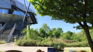 Una mesa con alimentos para el desayuno, incluyendo croissants, frutas y una bebida, ubicada al aire libre con vistas a un edificio moderno y zonas verdes.