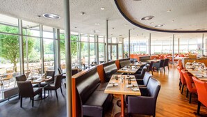 Un restaurante espacioso con techos altos, ventanas amplias y diversas opciones de asientos, incluyendo cabinas y mesas.