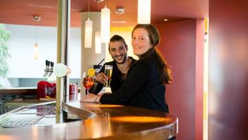Eine Bar mit einer Edelstahl-Theke, hängenden Pendelleuchten und einem roten Stuhl im Hintergrund.
