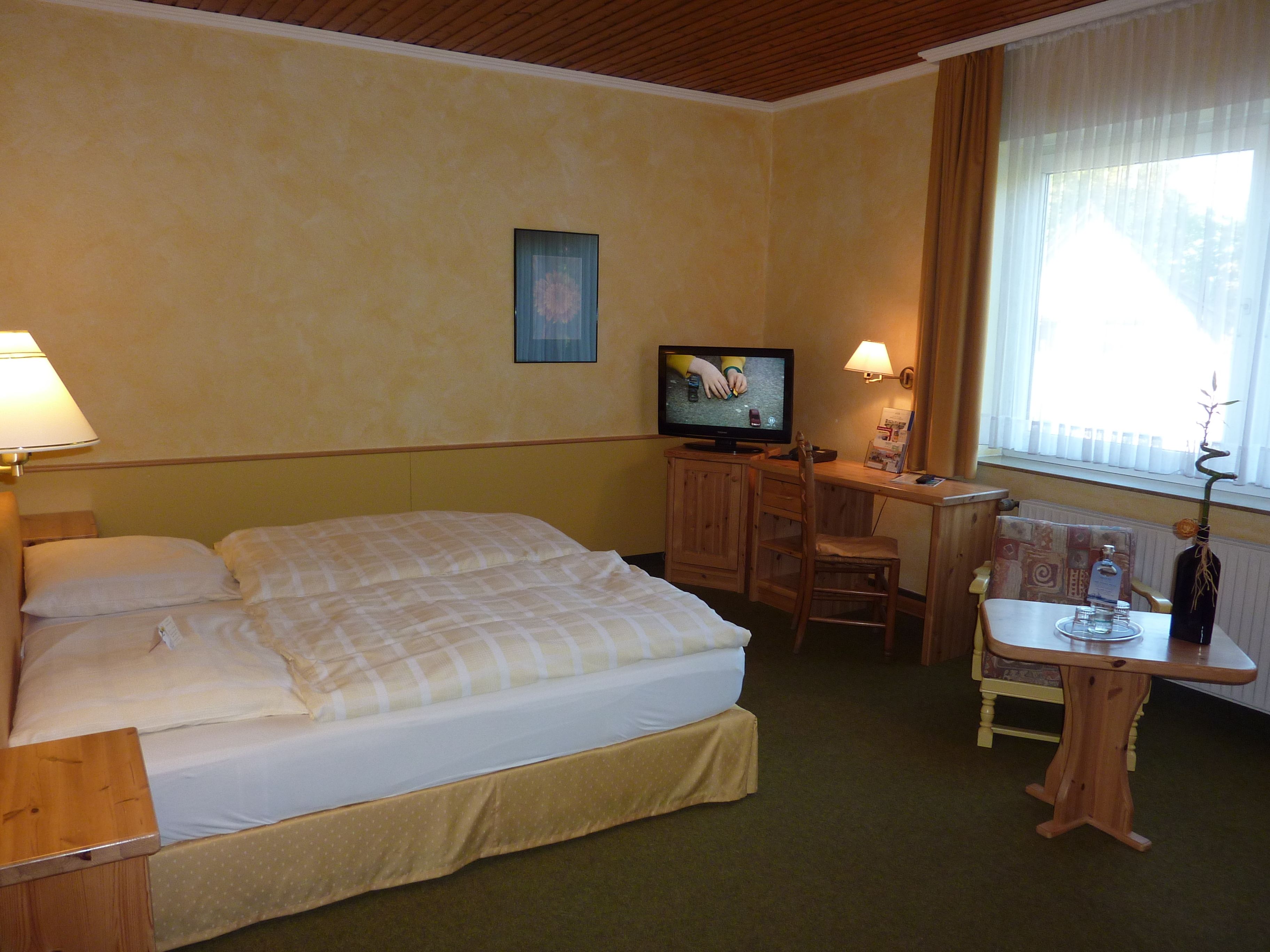 A hotel room with a bed, a desk with a chair, a television, and a window with curtains.