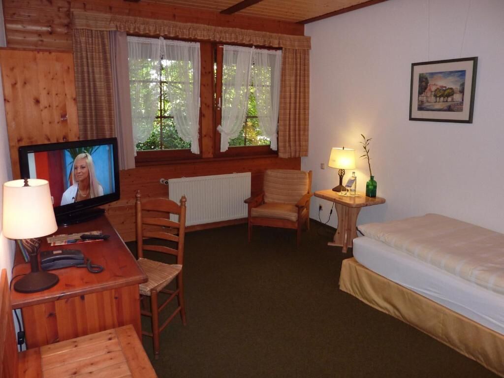 A cozy room with a wooden desk, a television, a chair, a bed, and a window with curtains.