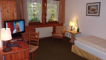 A cozy room with a wooden desk, a television, a chair, a bed, and a window with curtains.