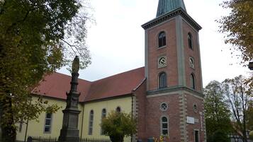 A church with a tall tower, a statue in front, and a well-maintained lawn.