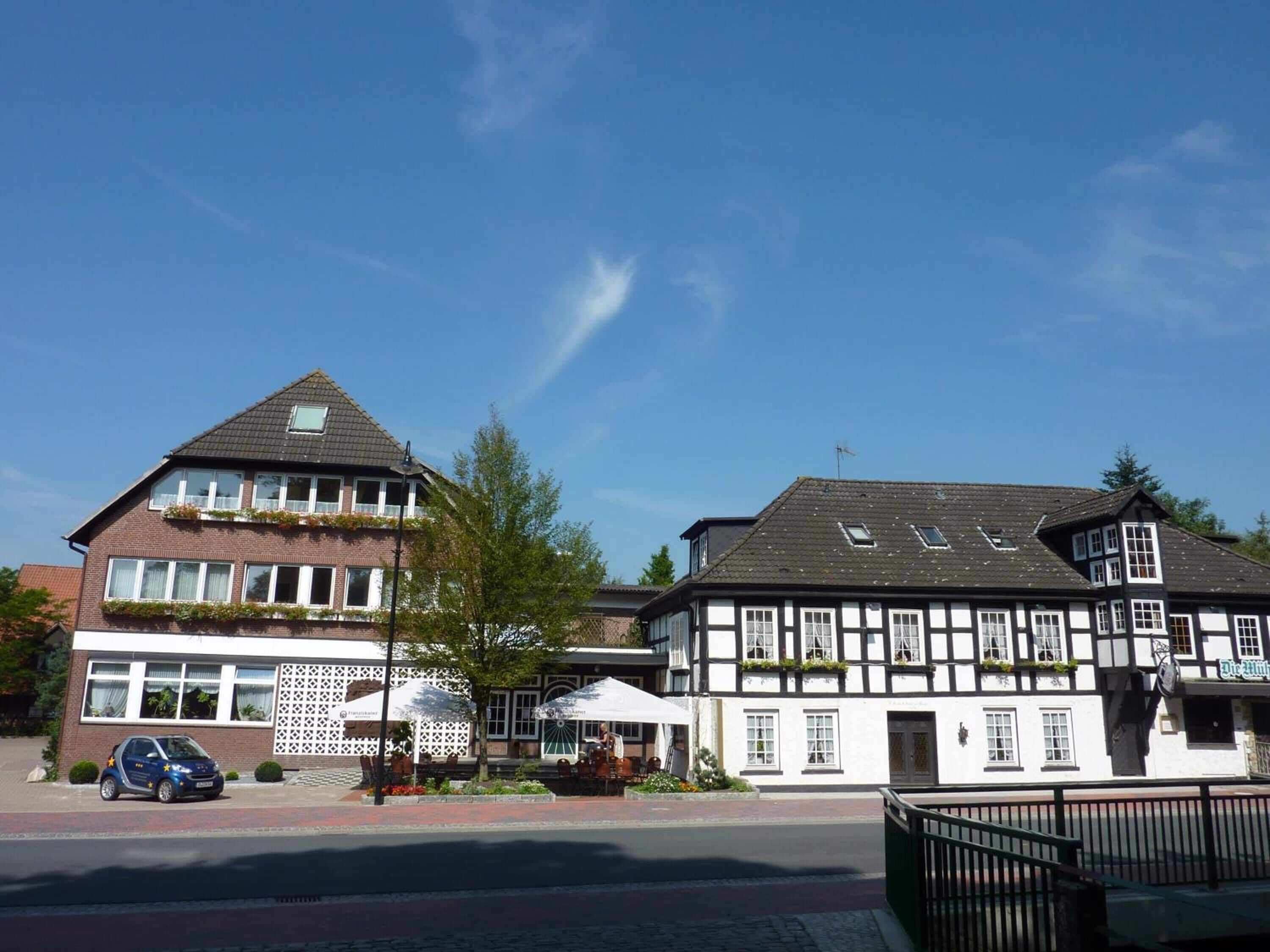 Un bâtiment européen traditionnel, avec une structure combinant des éléments en brique et en bois, une voiture garée devant et des places assises à l’extérieur.