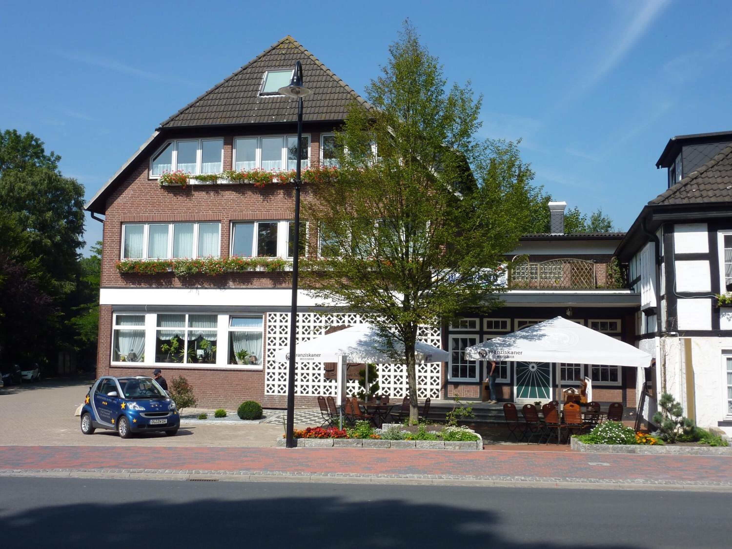 A two-story building with a brick facade, large windows, and a balcony with flower boxes.