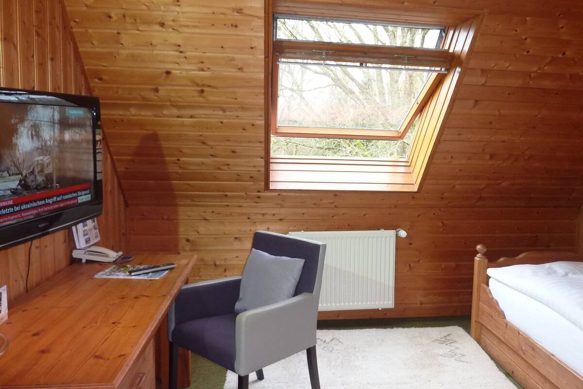 Une petite pièce agréable, avec un décor intérieur en bois, un bureau avec une chaise, un lit et une lucarne.