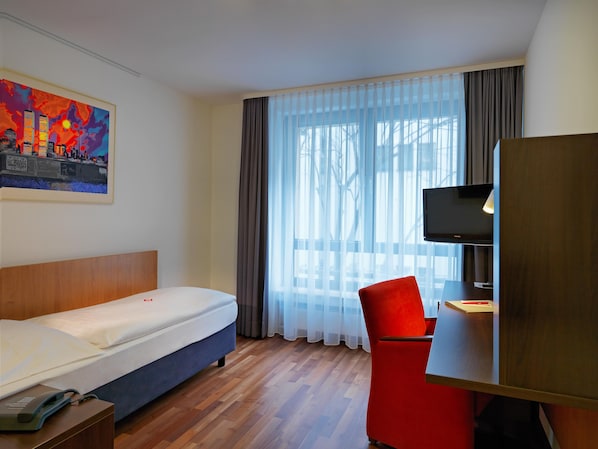 Habitación de hotel con cama, escritorio con silla, televisión y un cuadro en la pared.