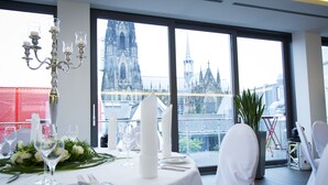 Une table à manger dressée pour un repas, avec vue sur une cathédrale par de grandes fenêtres.