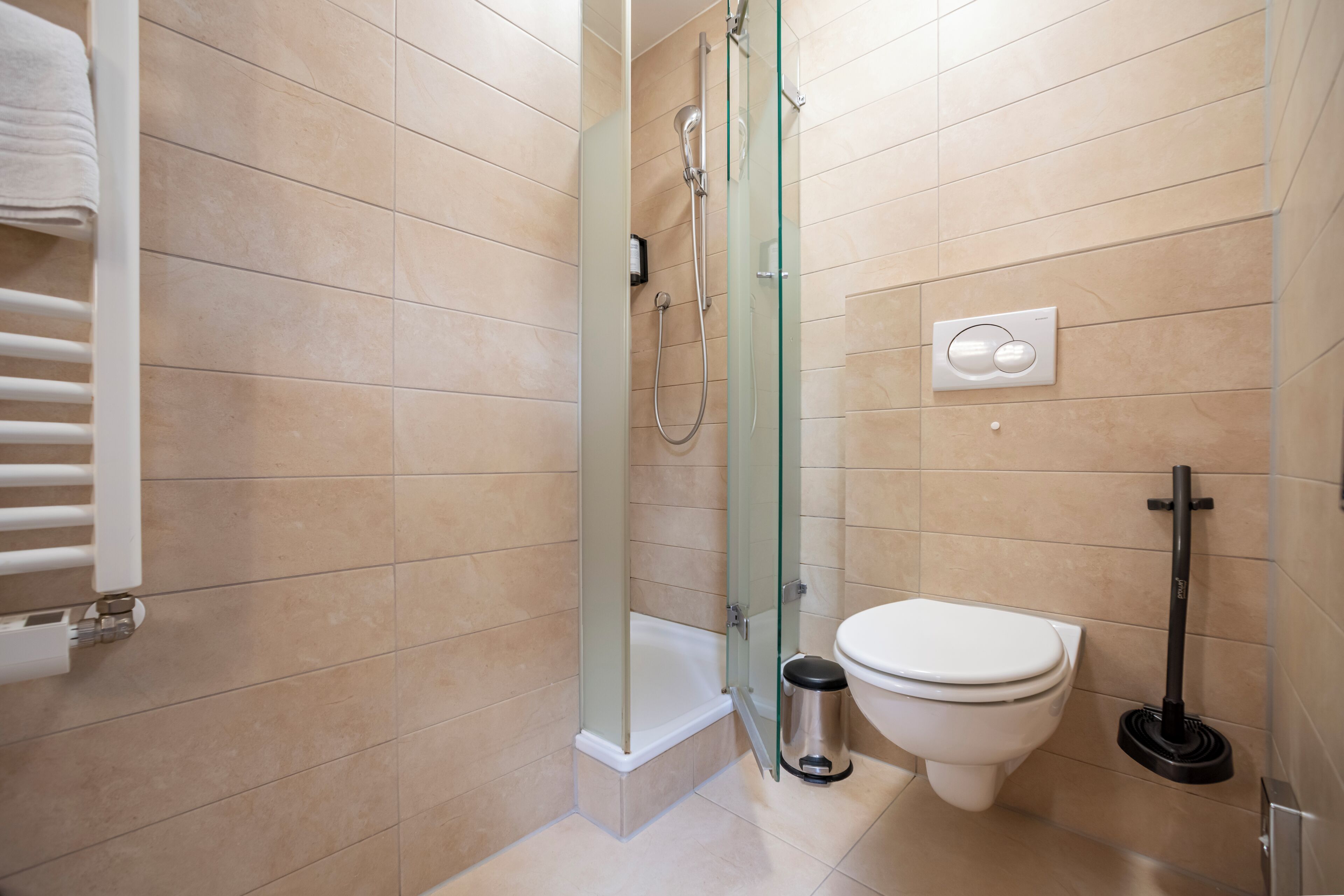 A bathroom with a glass-enclosed shower, a toilet, a trash bin, and a hand dryer.