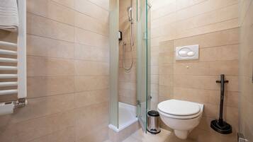 A bathroom with a glass-enclosed shower, a toilet, a trash bin, and a hand dryer.