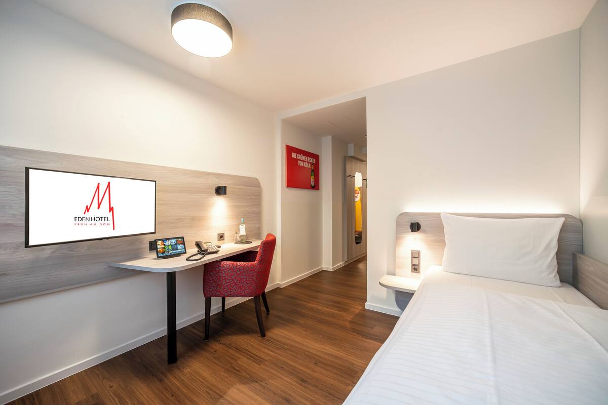 A hotel room with a bed, a desk with a chair, a TV, and a wall-mounted sign.