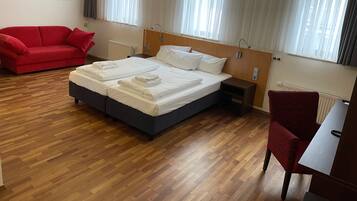 Una habitación de hotel con una cama, un sofá rojo, piso de madera y una ventana con cortinas.